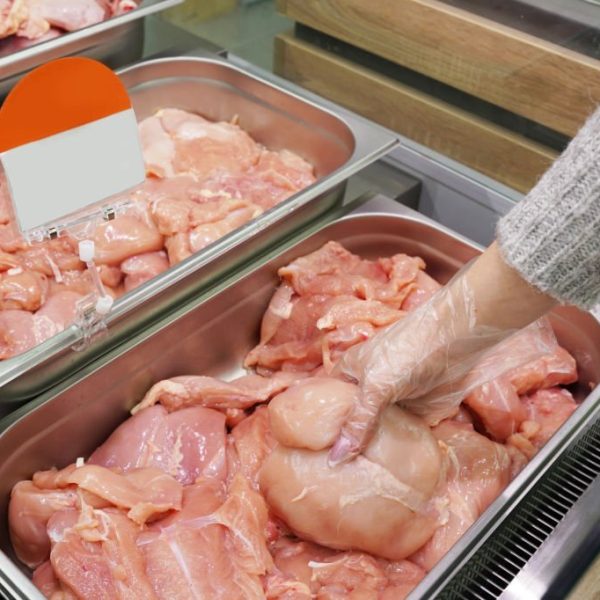Female hand holding fresh chicken fillet in a supermarket